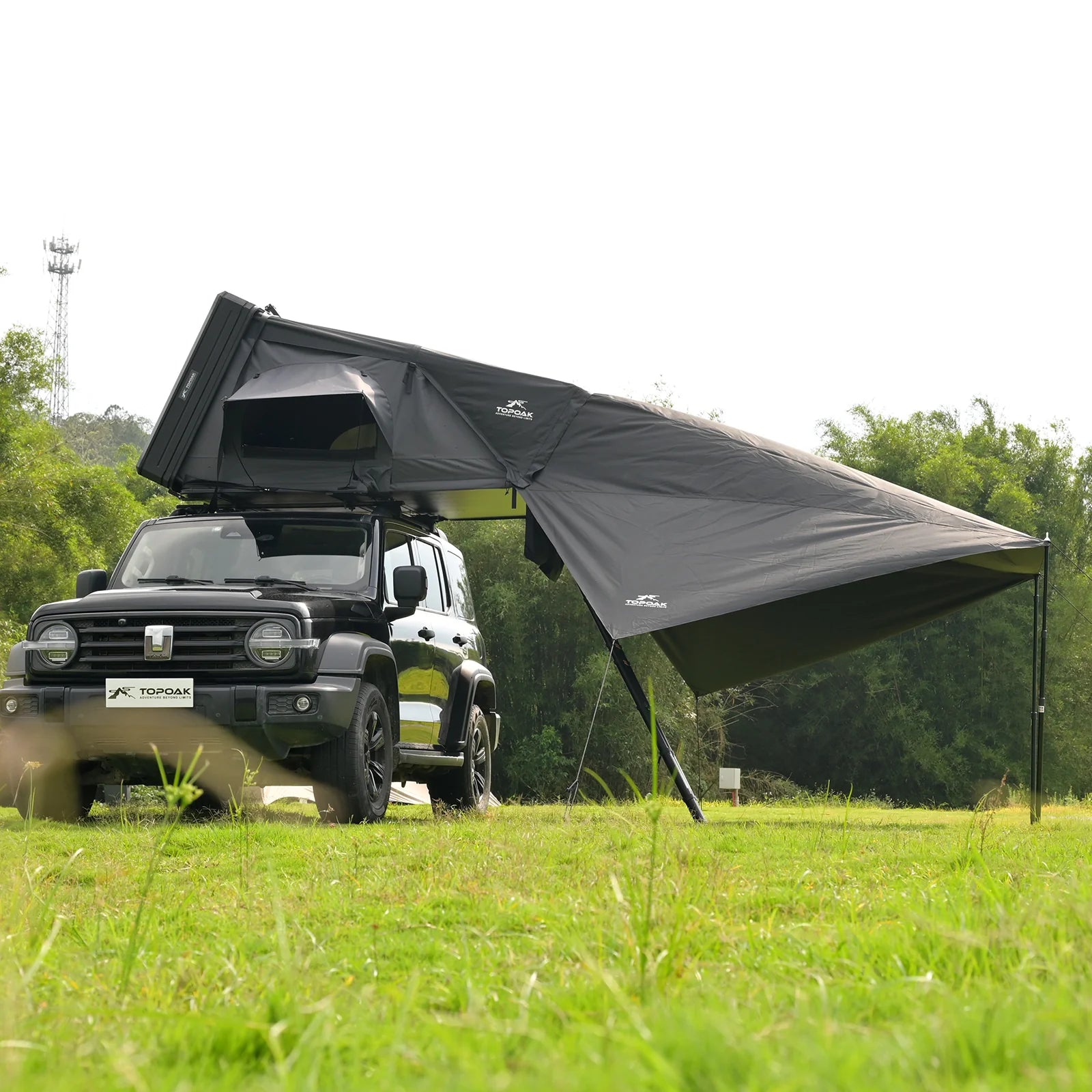 Black rooftop tent attached to a vehicle in a grassy outdoor setting with trees in the background.