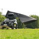 Black rooftop tent attached to a vehicle in a grassy outdoor setting with trees in the background.