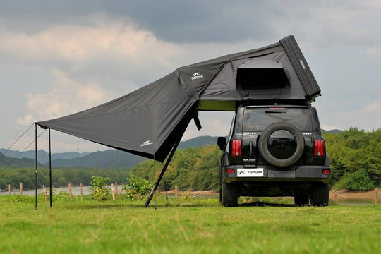 Black rooftop tent attached to a black SUV in a grassy field with mountains in the background.