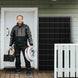 Man holding tools in front of a house with a solar panel on the wall.